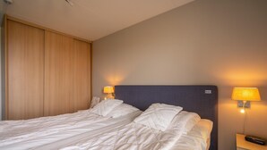 Ein Doppelbett mit weißen Leinen, zwei Nachttische mit Lampen und ein Holzkopfstück.