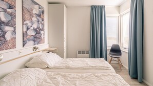 Quarto com cama, uma cadeira e duas pinturas na parede.