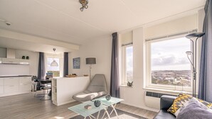 Sala moderna com sofá, mesa de centro de vidro e vista para a cidade através de grandes janelas.