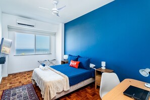 A bedroom with a bed, a desk, a chair, a window with a view of the sea, and a ceiling fan. - Luxury 3bdrs Sea View in Copacabana A 2440/515 (Rio de Janeiro)