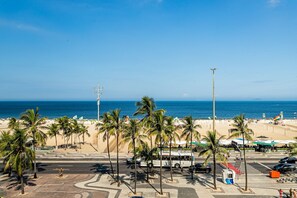 Vista sulla spiaggia con palme, un autobus e la spiaggia sullo sfondo.