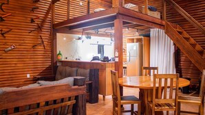 Interior de una cabaña de troncos con comedor, cocina y dormitorio en loft.