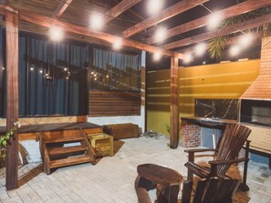 Un patio al aire libre con mobiliario de madera, una chimenea de ladrillo y un ventanal amplio.