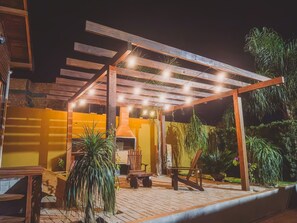 Un patio exterior con pérgola, asientos y una parrilla.