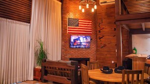 Un interior rústico con paredes de madera, un televisor fijado a la pared, una mesa de madera y un banco.