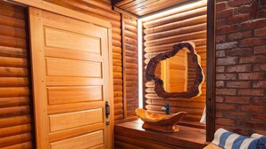 Interior de una cabaña de madera con puerta de madera, un lavabo de madera y un espejo en la pared.