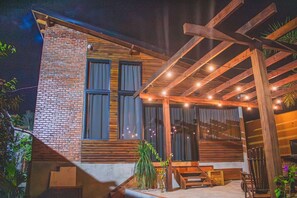 Un edificio moderno con fachada de ladrillo, ventanas amplias y una pérgola de madera con luces colgantes.