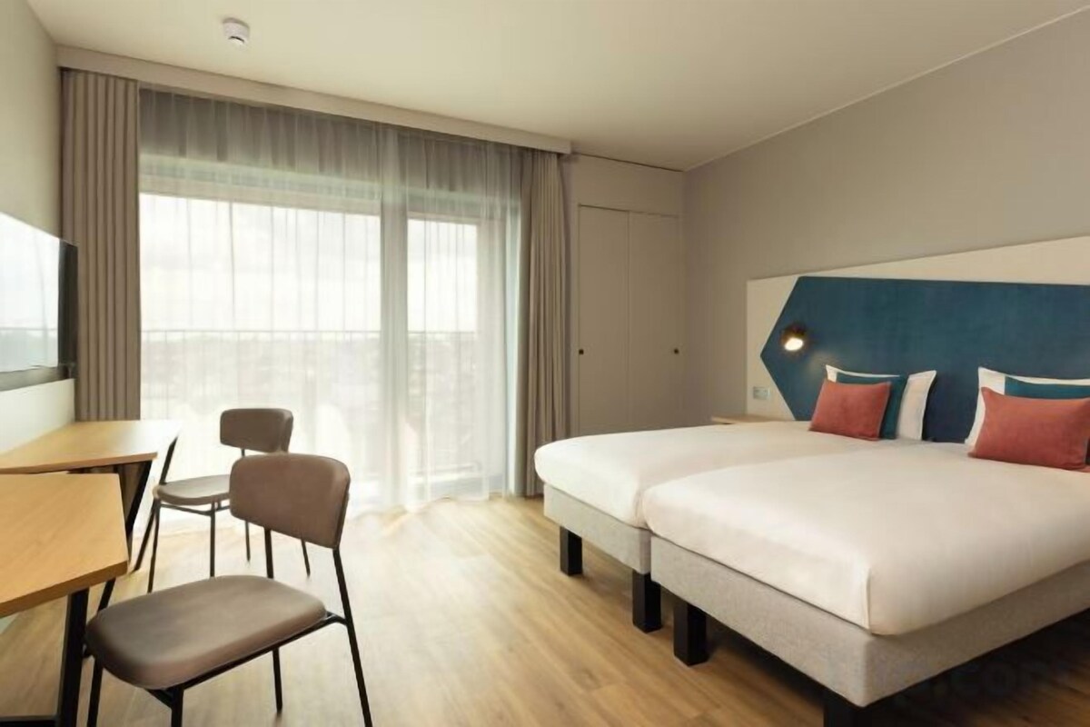 Ein Hotelzimmer mit Bett, Schreibtisch, Stuhl und einem großen Fenster.