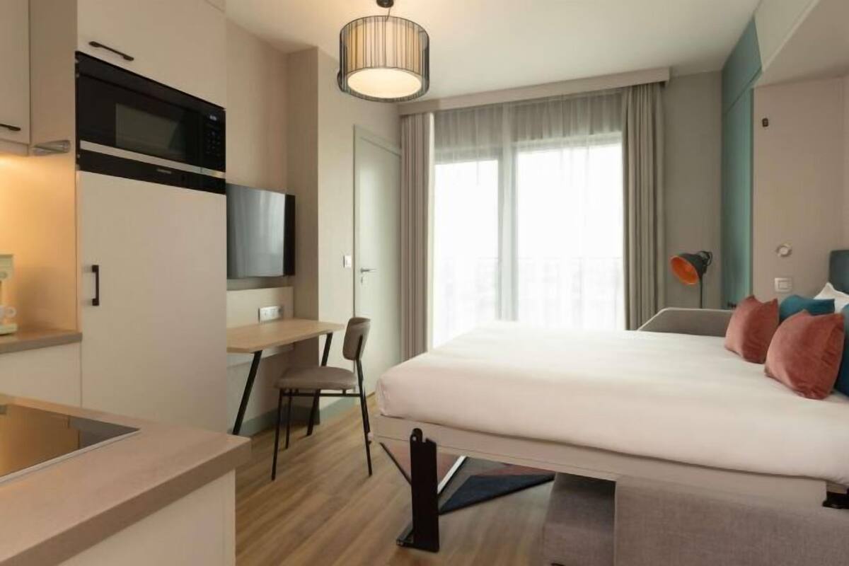 Habitació d'hotel moderna amb llit, escriptori i petita cuina.
