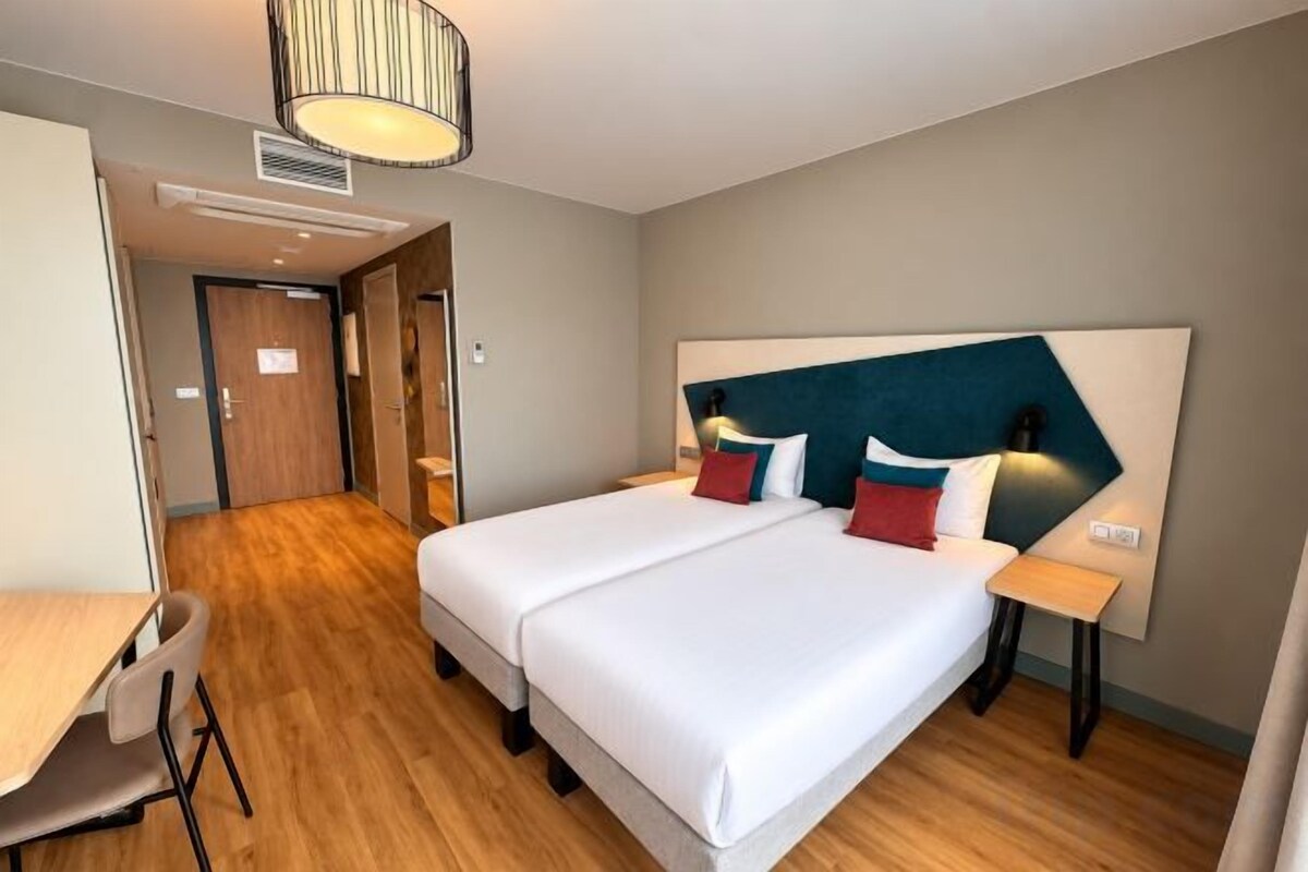 Ein Hotelzimmer mit Doppelbett, Nachttischen, einem Schreibtisch und einem Sessel.