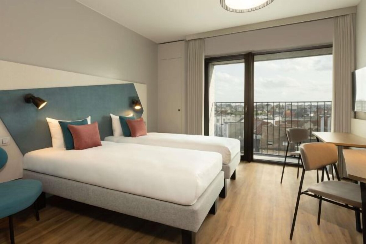 Ein Hotelzimmer mit zwei Betten, einem Balkon, einem Essbereich und Blick auf die Stadt.