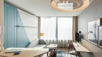 Ein modernes Hotelzimmer mit einer Couch, zwei Tischen, einem Fernseher und einem großen Fenster mit Vorhängen.