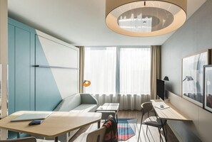 A modern hotel room with a sofa, two tables, a TV, and a large window with curtains. - Aparthotel Adagio Antwerp City Center (Antwerp)