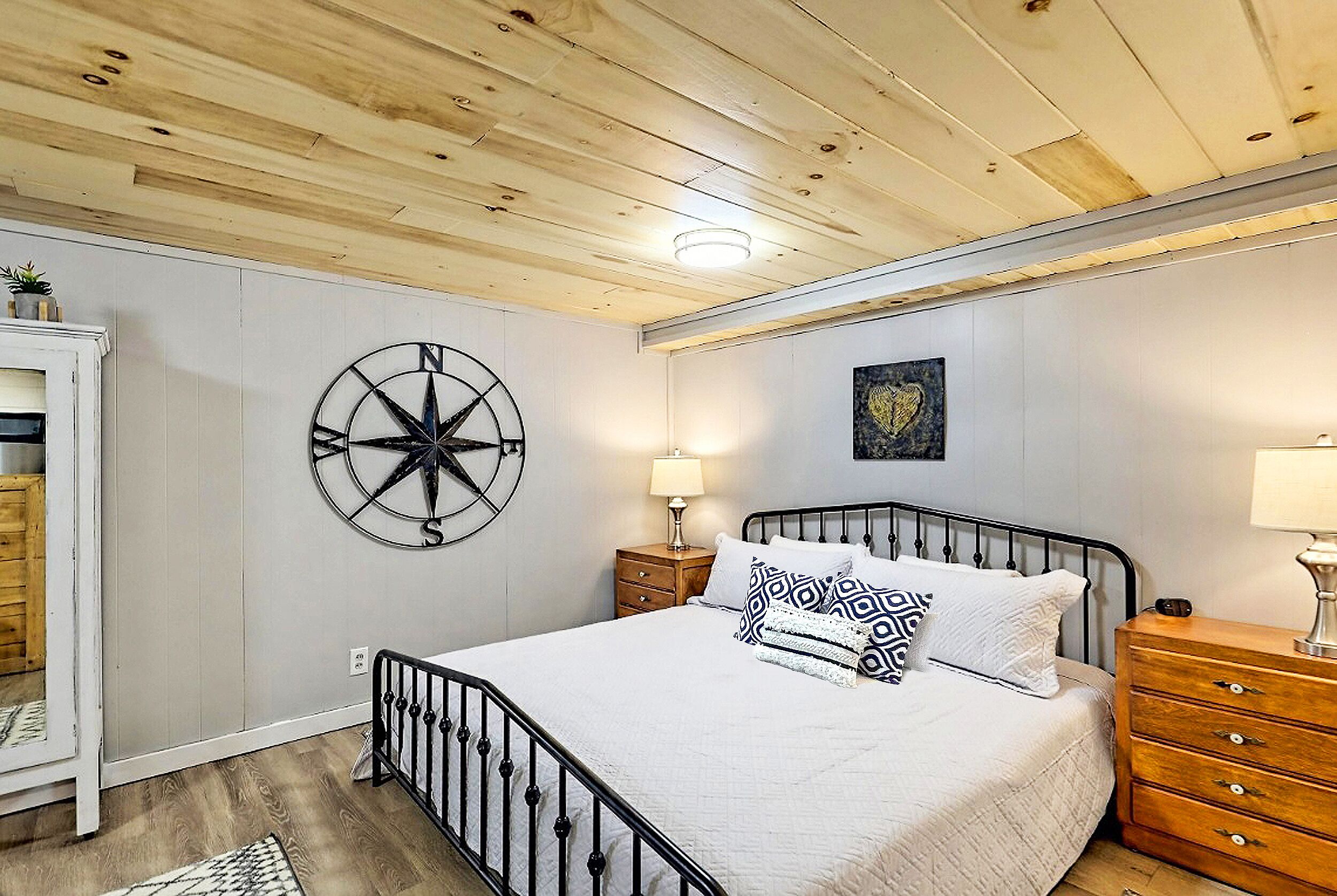 A bedroom with a bed, a compass wall decoration, a wooden dresser, and a nightstand with a lamp.