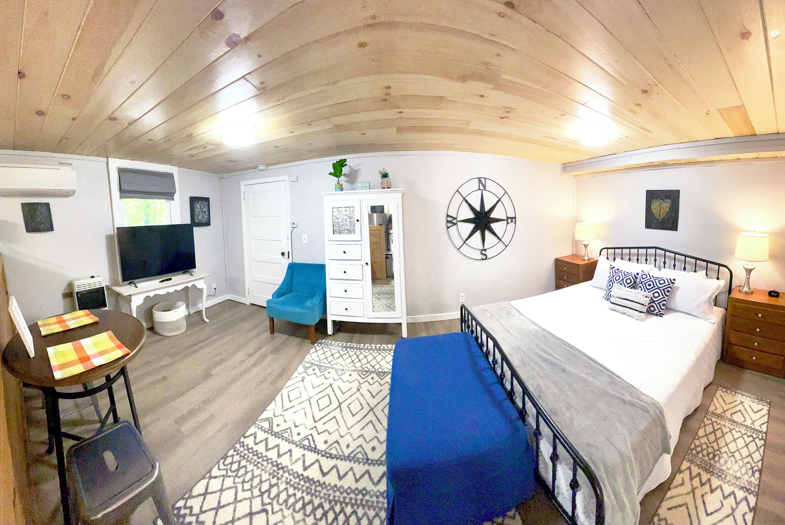 Een slaapkamer met een bed, een bureau, een stoel, een televisie, een kledingkast en een kompasdecoratie aan de muur.
