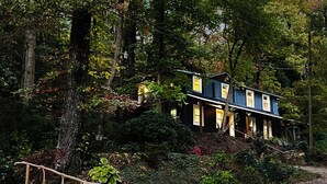 Una casa de dues plantes amb un teulat molt inclinat, envoltada de bosc dens.