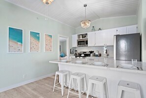 A modern kitchen with white bar stools, a stainless steel refrigerator, and a white countertop.
