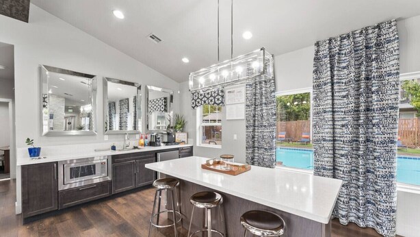 A modern kitchen with a central island, bar stools, and a view of a swimming pool.