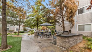 An outdoor patio area with a grill, dining table, chairs, and a covered seating area.