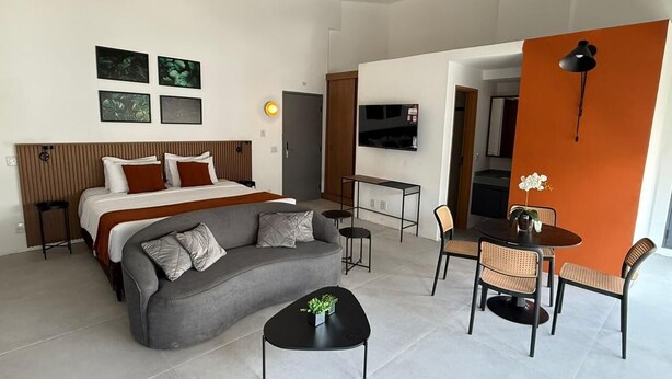 A modern hotel room with a bed, sofa, dining table, chairs, and a TV. - Heritage X (São Paulo)