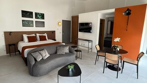A modern hotel room with a bed, sofa, coffee table, dining area, and TV. - Heritage X (São Paulo)
