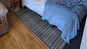 A small, cozy room with a wooden ceiling and walls, a single bed with a patterned blanket, a bedside lamp, and a small wooden nightstand. - Suite 9 - Older/Simple/Rustic/No Frills/Budget 1 Bed - Near Cabot Beach Park (Kensington)