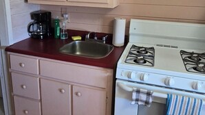 A compact kitchen with wooden cabinets, a gas stove, a sink, and a coffee maker. - Suite 9 - Older/Simple/Rustic/No Frills/Budget 1 Bed - Near Cabot Beach Park (Kensington)