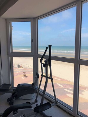 A gym with exercise equipment and a view of the beach through large windows. - Villaloha, luxury home on the sea wall. (Bray-Dunes)