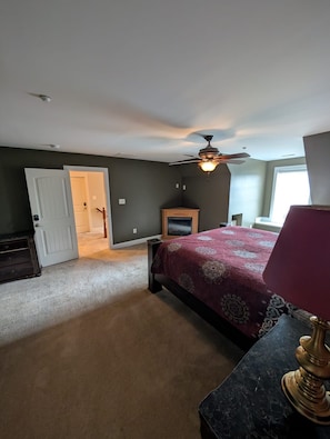A bedroom with a bed, a ceiling fan, a nightstand, and a door leading to another room. - Renewal Room at the Hilltop Hideaway King Bed (Hampstead)