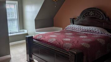 Un dormitorio con techo inclinado, ventilador de techo, cama con colcha estampada y ventana con persianas.