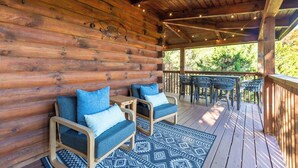Eine überdachte Veranda mit Holzwänden, zwei gepolsterte Stühle mit blauen Kissen und einem gemusterten Teppich.