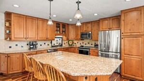 Eine Küche mit Holzschränken, Granit Arbeitsplatten, Edelstahlgeräten und einer Kochinsel mit Barhocker.