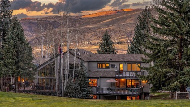 Ein zweigeschossiges Haus mit Balkon, umgeben von Bäumen und einer hügeligen Landschaft.