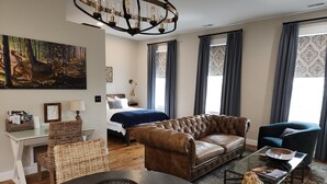 A modern bedroom with a large bed, a brown leather sofa, a blue armchair, a dining table with a basket, and a chandelier. - 2nd Street Loft - Riverview (Washington)