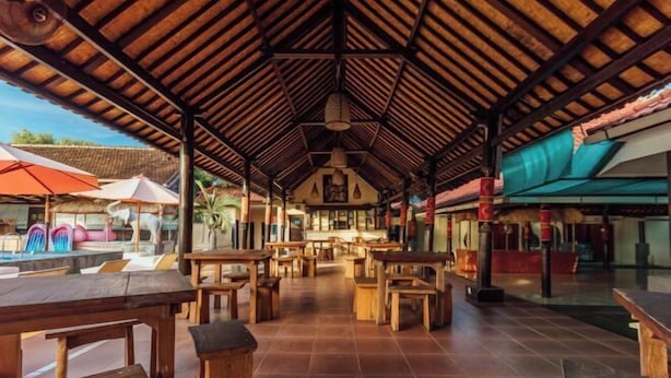 An open-air restaurant with wooden tables and chairs, a tiled floor, and a thatched roof. - Semaya One Beach Hotel (Bali)