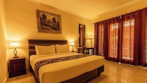 A hotel room with a bed, two bedside tables, a nightstand, a mirror, and a window with curtains. - Semaya One Beach Hotel (Bali)
