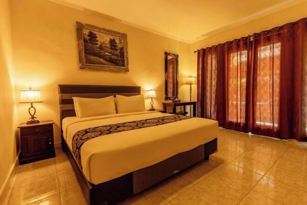 Une chambre d’hôtel avec un lit, deux tables de chevet, une commode, un miroir et une fenêtre avec des rideaux.