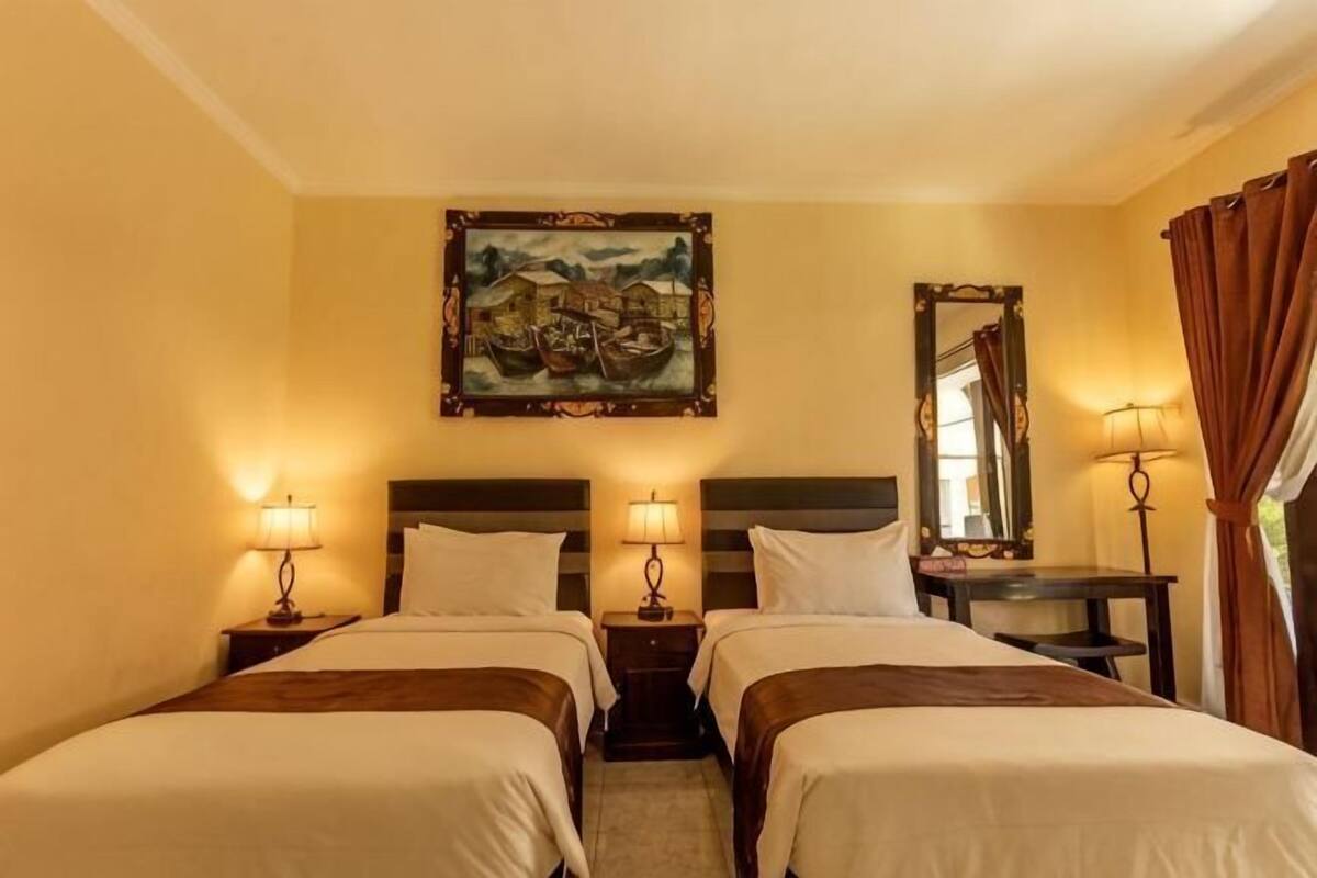 Une chambre d’hôtel avec deux lits, un tableau au mur, un miroir et une table avec une lampe.