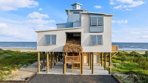 Ein zweistöckiges Strandhaus mit einem Strohdach, einer Holzterrasse und Blick auf den Ozean.