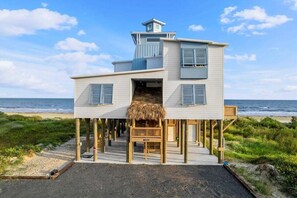 A two-story beachfront house with a thatched-roof structure, wooden deck, and a view of the ocean. - Beachfront | Hot Tub | Sleeps 20 (Crystal Beach)