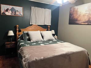 A bed with a wooden headboard, two bedside tables with lamps, a checkered curtain, and a framed picture on the wall.