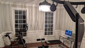 Ein Heimfitnessraum mit Trainingsgeräten, einem großen Fenster und einem Computermonitor.