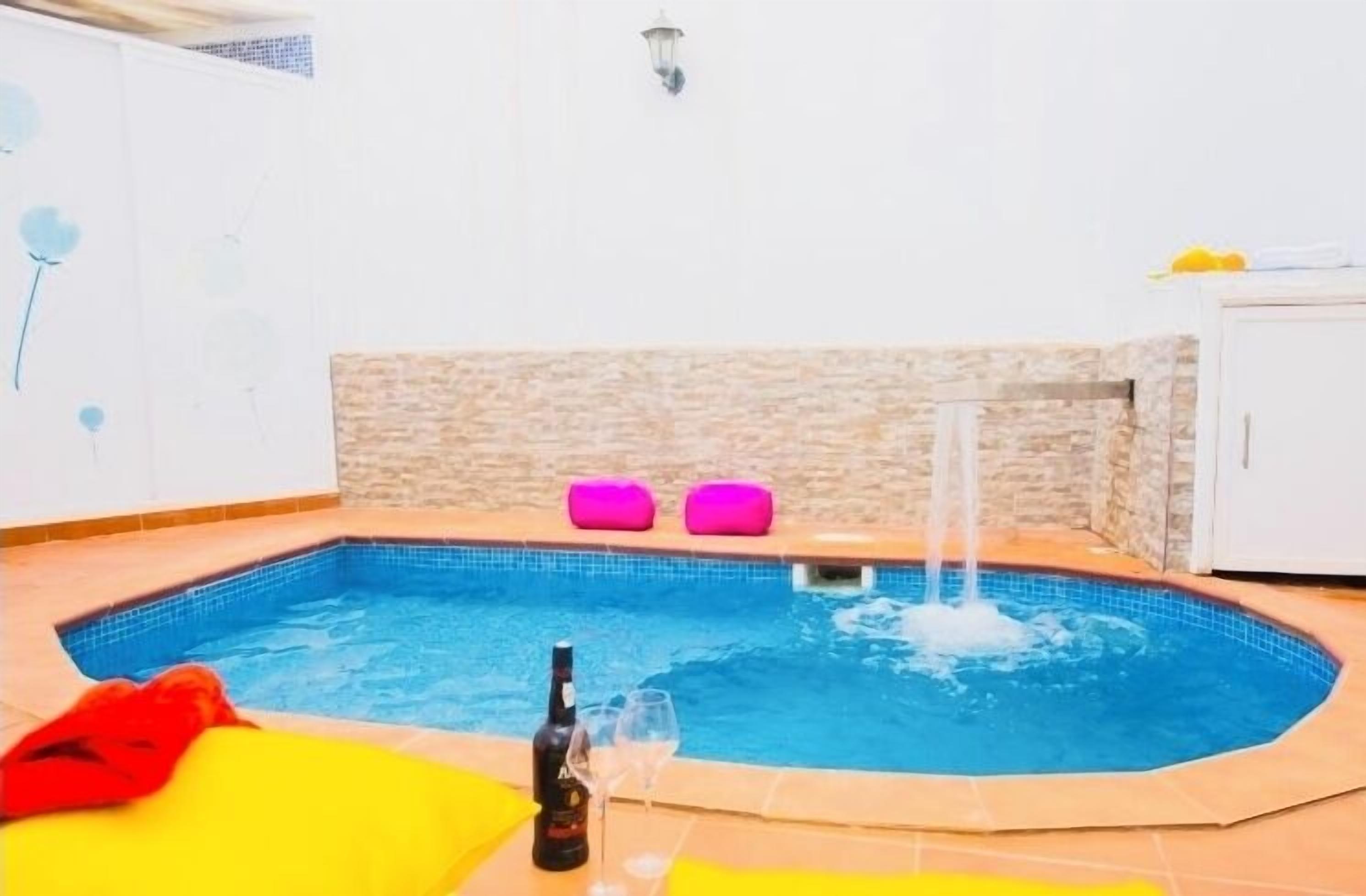 Un bain à remous avec un mur de pierres en arrière-plan, une bouteille et deux verres posés sur le bord.