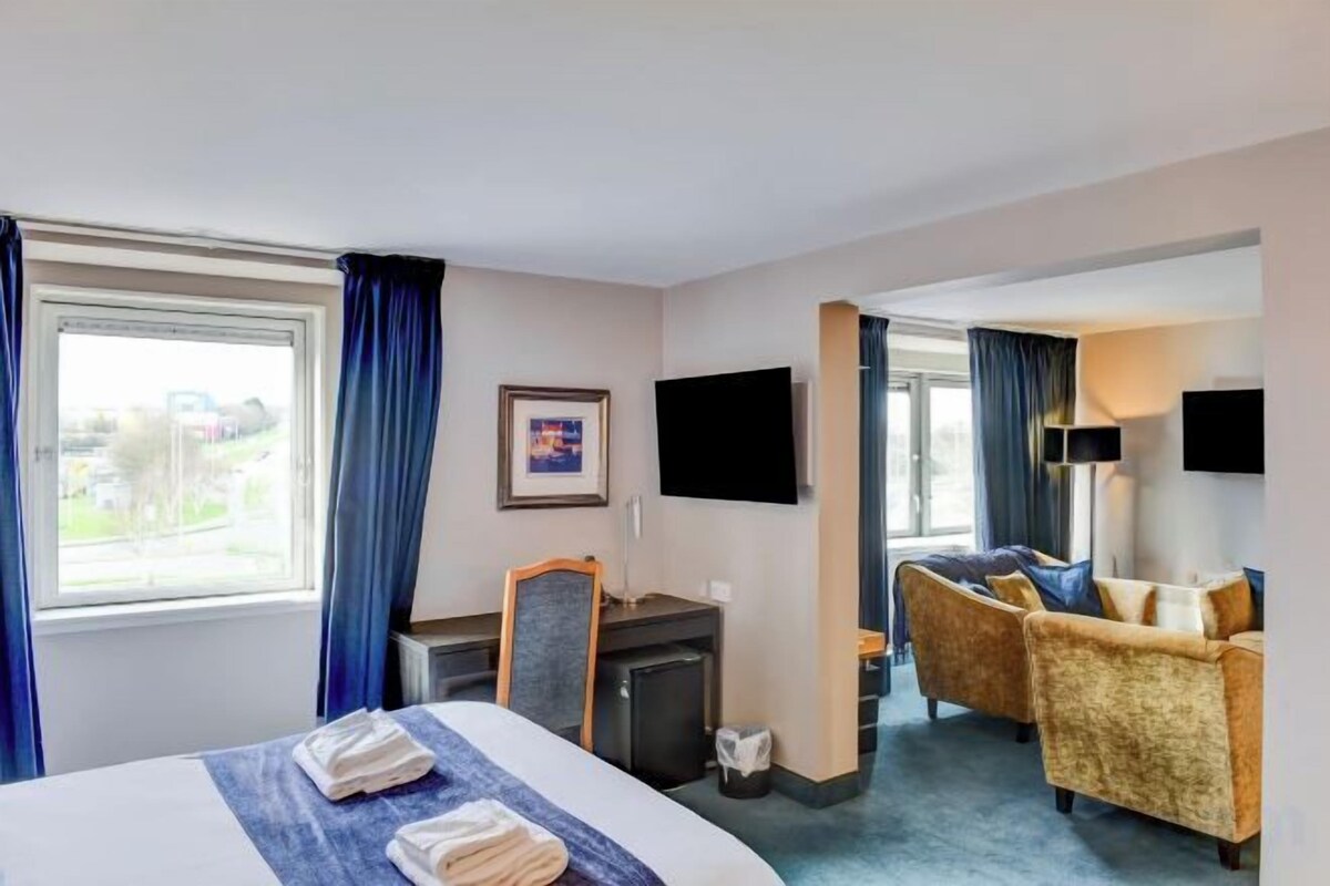Habitación de hotel con cama, escritorio, televisión y zona de estar.
