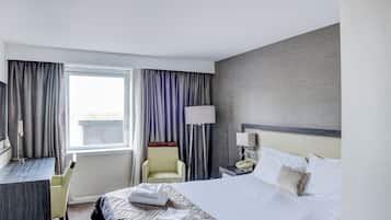 Habitación de hotel con cama, escritorio, silla, lámpara y ventana con cortinas.