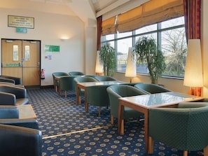 Une salle de conférence d’hôtel avec un tapis à motifs bleus, des chaises recouvertes d’un tissu vert, une table en bois et de grandes fenêtres avec des rideaux.