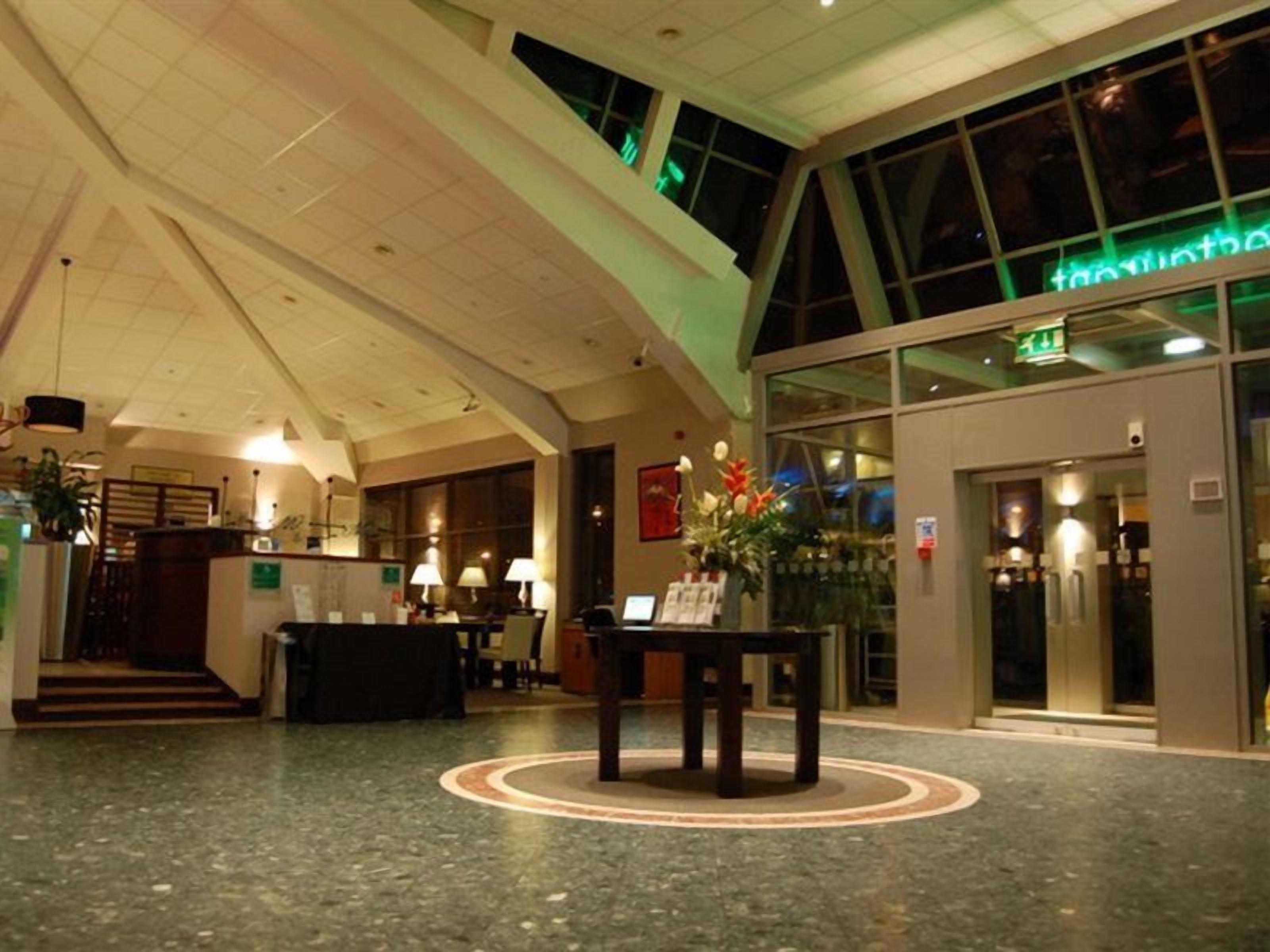 A hotel lobby with a reception desk, a staircase, and a large window.