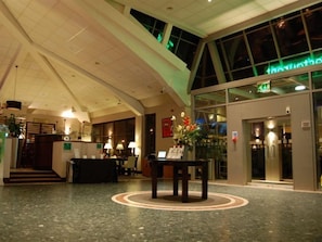Un hall d’hôtel avec un comptoir d’accueil, un escalier et une grande fenêtre.