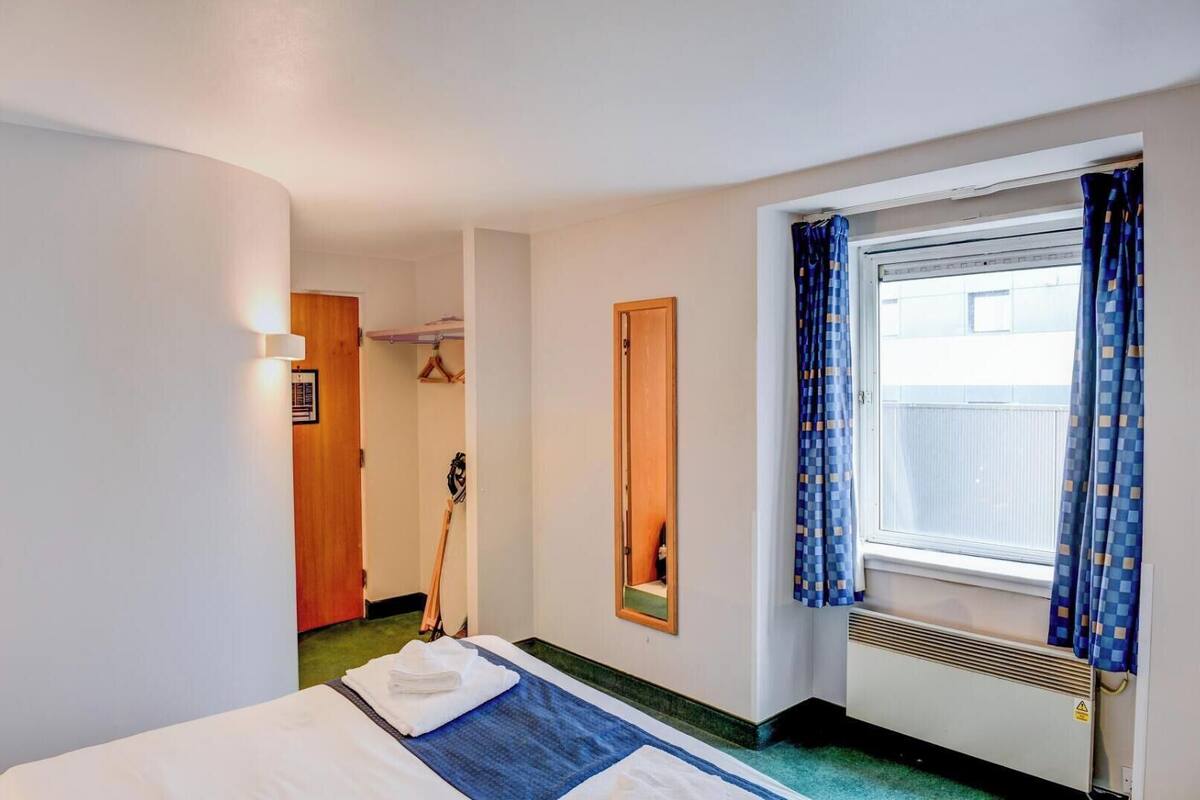 Ein Hotelzimmer mit Bett, einem Vorhangfenster, einem Spiegel und einem Kleiderständer.