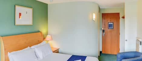 A hotel room with a bed, a nightstand, a lamp, a door, and a chair.